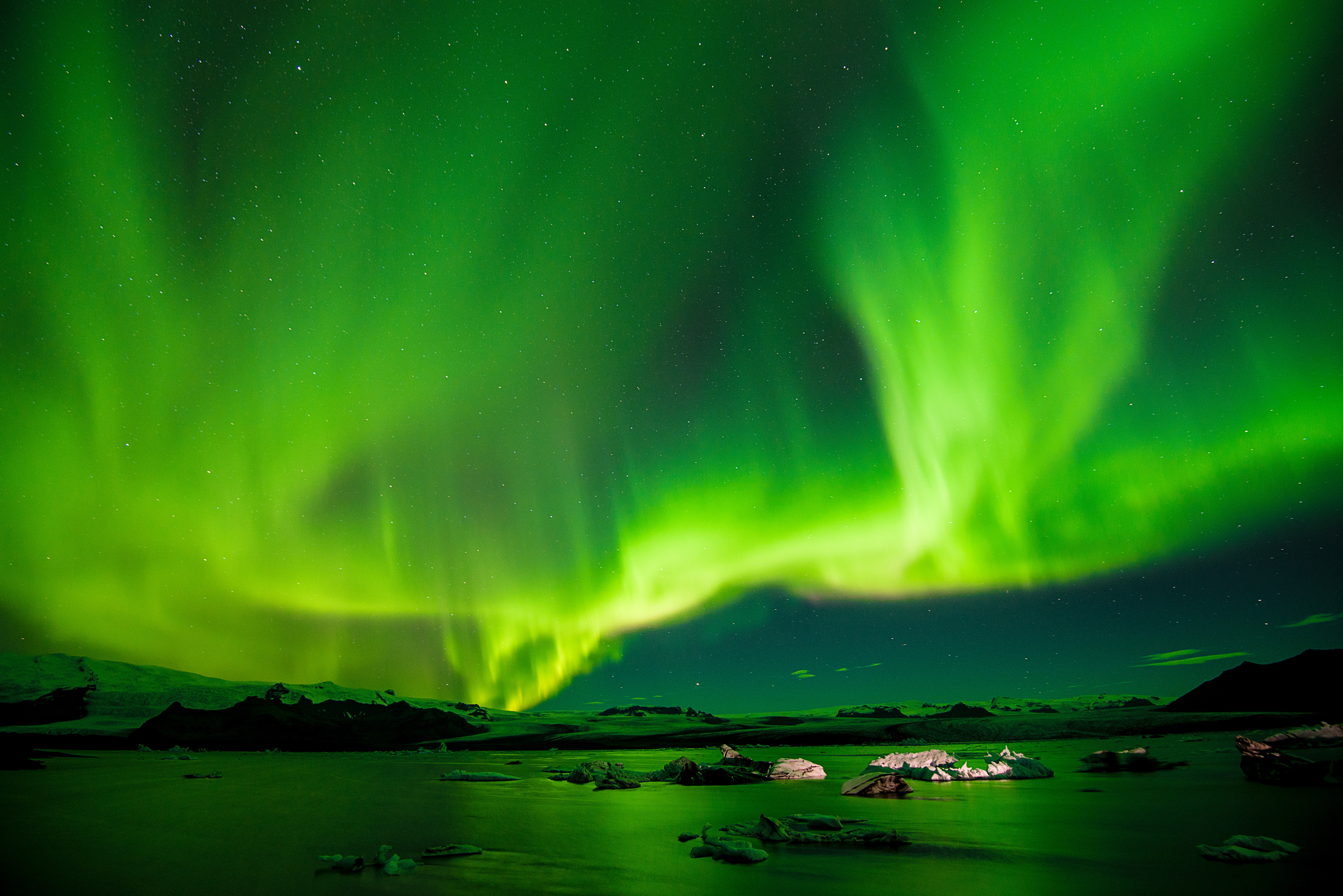 A bright green aurora borealis curving above a snowy place.