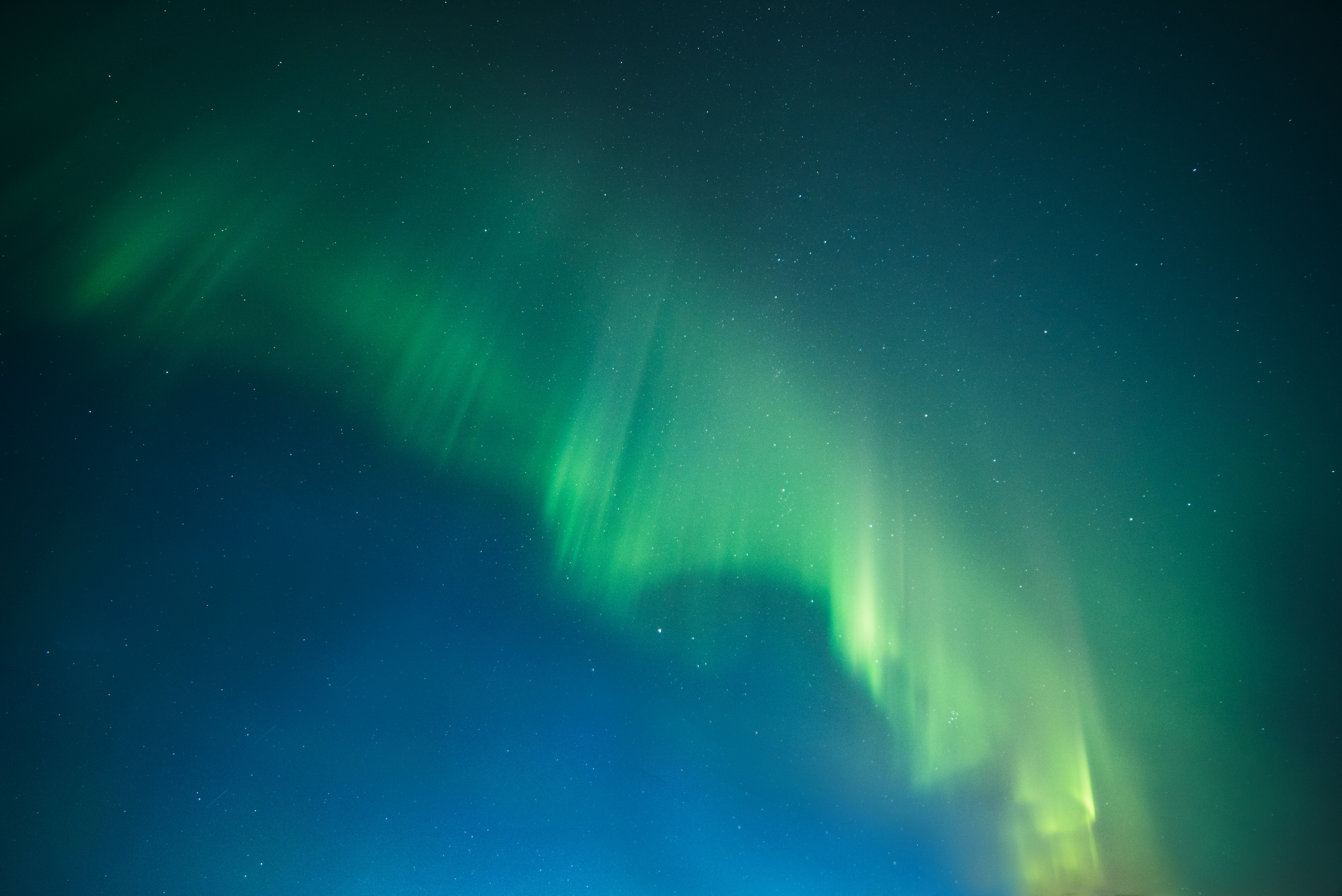 Photo of a green aurora borealis against a blue night sky