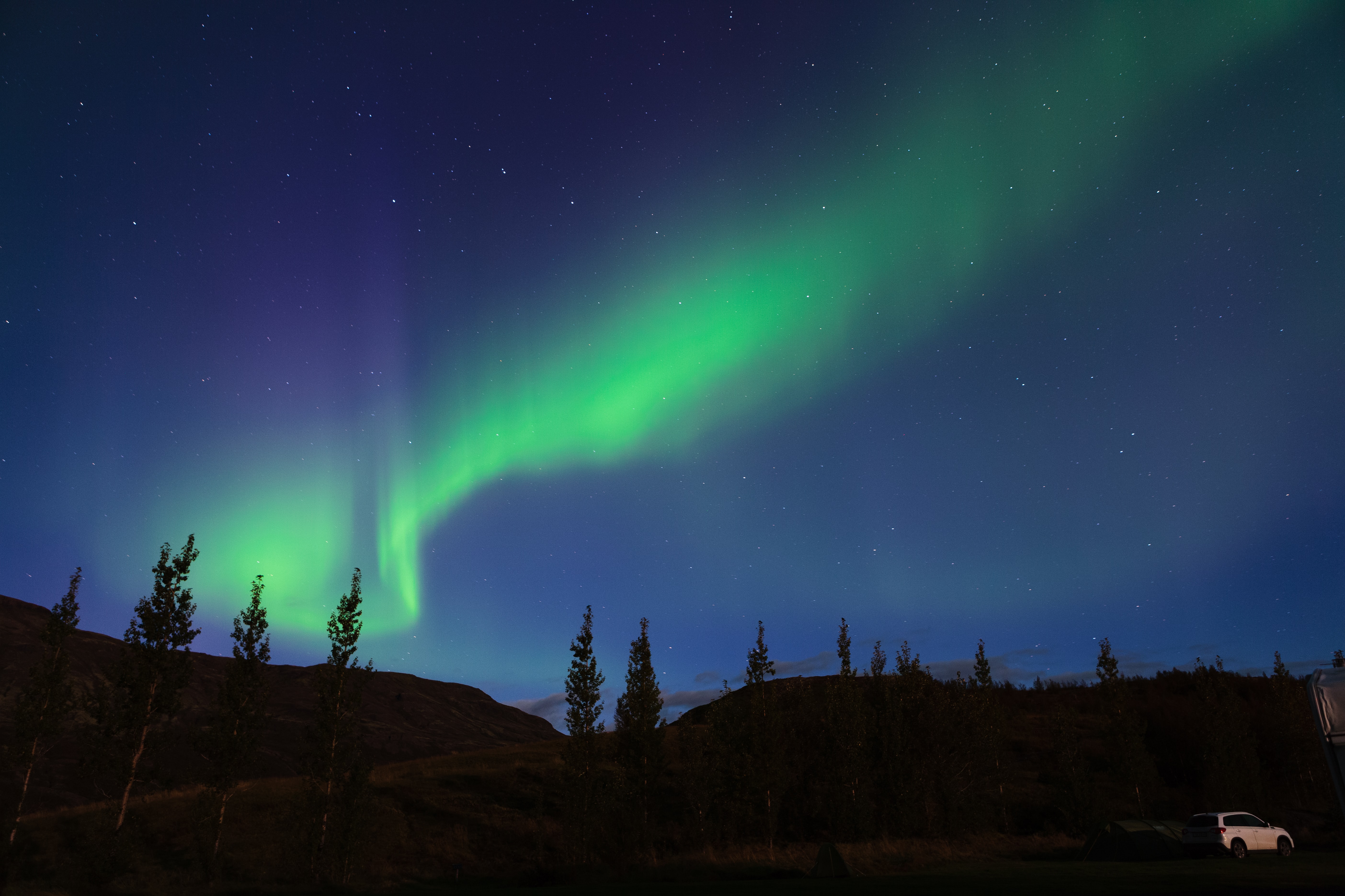 A green slightly curved aurora borealis over hills.